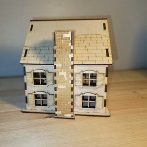 May include: A wooden model of a house with a brown brick chimney, a brown roof, and four windows with white frames. The house is sitting on a wooden surface.