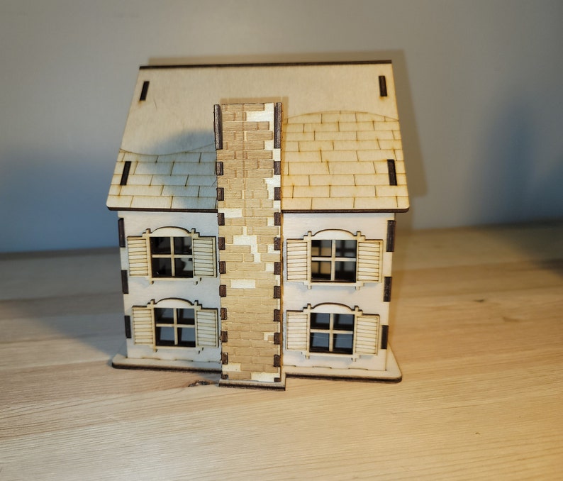 May include: A wooden model of a house with a brown brick chimney, a brown roof, and four windows with white frames. The house is sitting on a wooden surface.