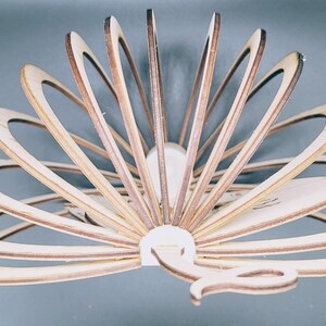 May include: A wooden peacock sculpture with a fan-like tail made of layered wood pieces. The sculpture is painted in shades of brown and beige.