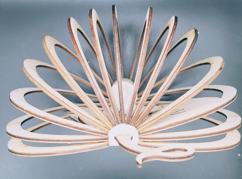 May include: A wooden peacock sculpture with a fan-like tail made of layered wood pieces. The sculpture is painted in shades of brown and beige.