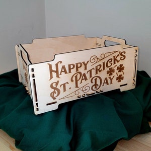 Puede incluir: Una caja de madera con un diseño recortado y el texto "Happy St. Patrick's Day" con tréboles. La caja está sobre una superficie de tela verde.