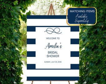 Op de afbeelding: Een marineblauw en wit gestreept welkomstbord op een houten ezel. Het bord leest "Welkom bij Amelia's Bridal Shower" met een nautisch touwknooppatroon. Het bord bevat ook de datum "Zondag 20 juli 20XX".