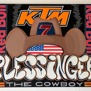 May include: A black and orange KTM logo with a brown cowboy hat with a red and blue number 7 patch on top. The hat is over a white and red American flag. The words "Red Bull" are on the left and right sides of the image. Below the hat is the word "PLESSINGER" in white with orange outlines. Below that is the text "THE COWBOY" in silver with orange outlines.
