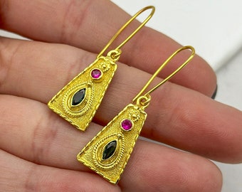 Peut inclure: Boucles d'oreilles pendantes dorées de forme triangulaire. Les boucles d'oreilles sont ornées de pierres précieuses noires et roses.