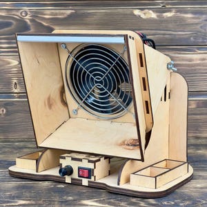 Könnte beinhalten: Eine Holzstaubsammelbox mit einem Ventilator und einem Licht. Die Box hat ein kleines Fach unten mit einem Netzschalter und einem Kabel.