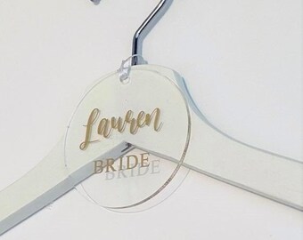 May include: White wooden hanger with a clear round acrylic tag that says "Lauren Bride" in gold lettering.