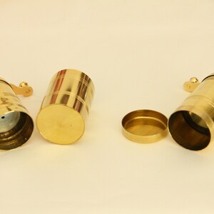 May include: Three gold metal spice grinders with a handle on the side. One grinder is open, showing the inside.