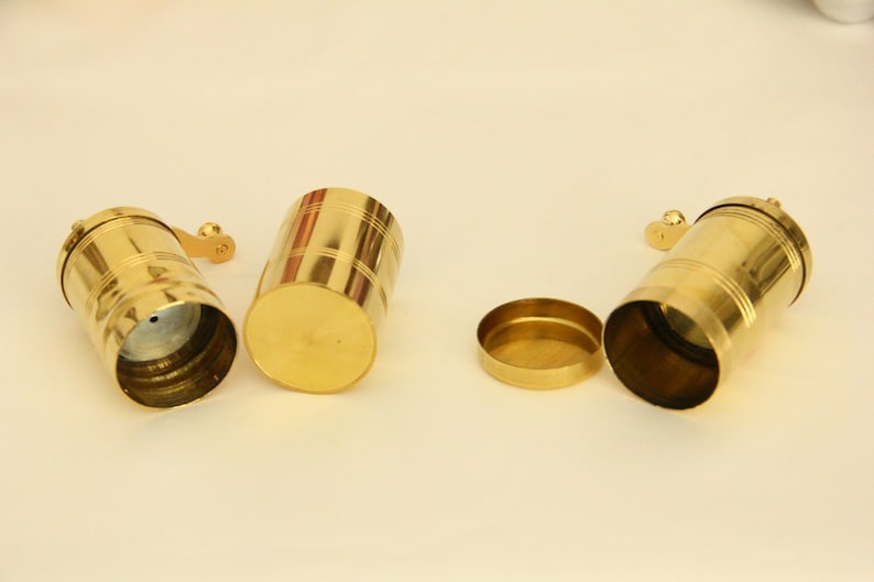 May include: Three gold metal spice grinders with a handle on the side. One grinder is open, showing the inside.