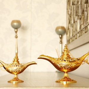 Peut inclure: Deux lampes &agrave; genie dor&eacute;es avec des motifs complexes et des d&eacute;tails orn&eacute;s. Les lampes sont sur une surface brun clair.