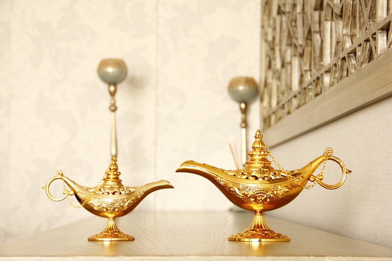 Peut inclure: Deux lampes &agrave; genie dor&eacute;es avec des motifs complexes et des d&eacute;tails orn&eacute;s. Les lampes sont sur une surface brun clair.