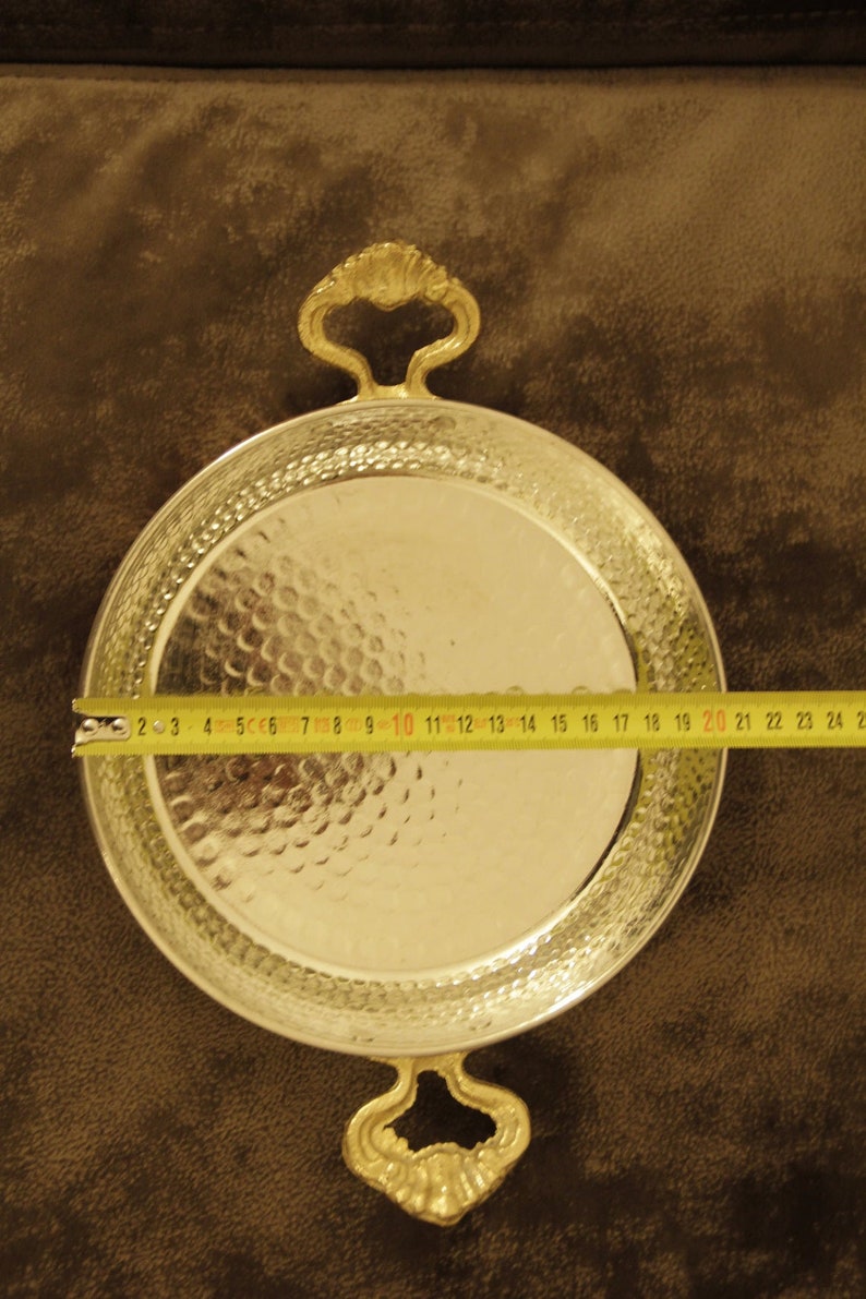 May include: A silver serving tray with two ornate gold handles. The tray is 20 inches in diameter and has a hammered finish.