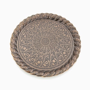 May include: A round, copper-colored tray with a decorative, intricate design. The design features a repeating pattern of floral motifs and swirls. The tray has a raised edge and a smooth, polished surface. Vintage Serving Tray, Round Tray, Vintage Tray, Decorative Tray
