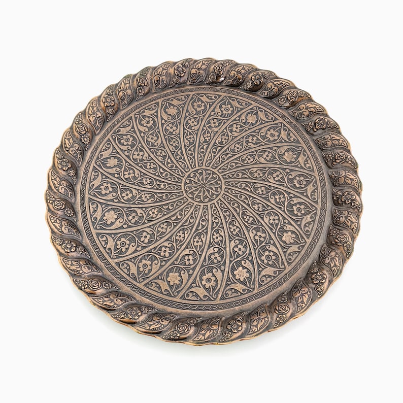 May include: A round, copper-colored tray with a decorative, intricate design. The design features a repeating pattern of floral motifs and swirls. The tray has a raised edge and a smooth, polished surface. Vintage Serving Tray, Round Tray, Vintage Tray, Decorative Tray