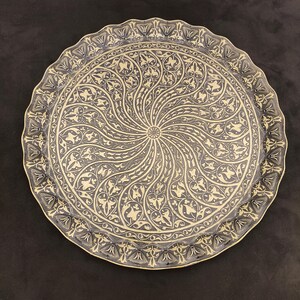 May include: A round, brass serving tray with a decorative, swirling pattern of black and gold floral designs.