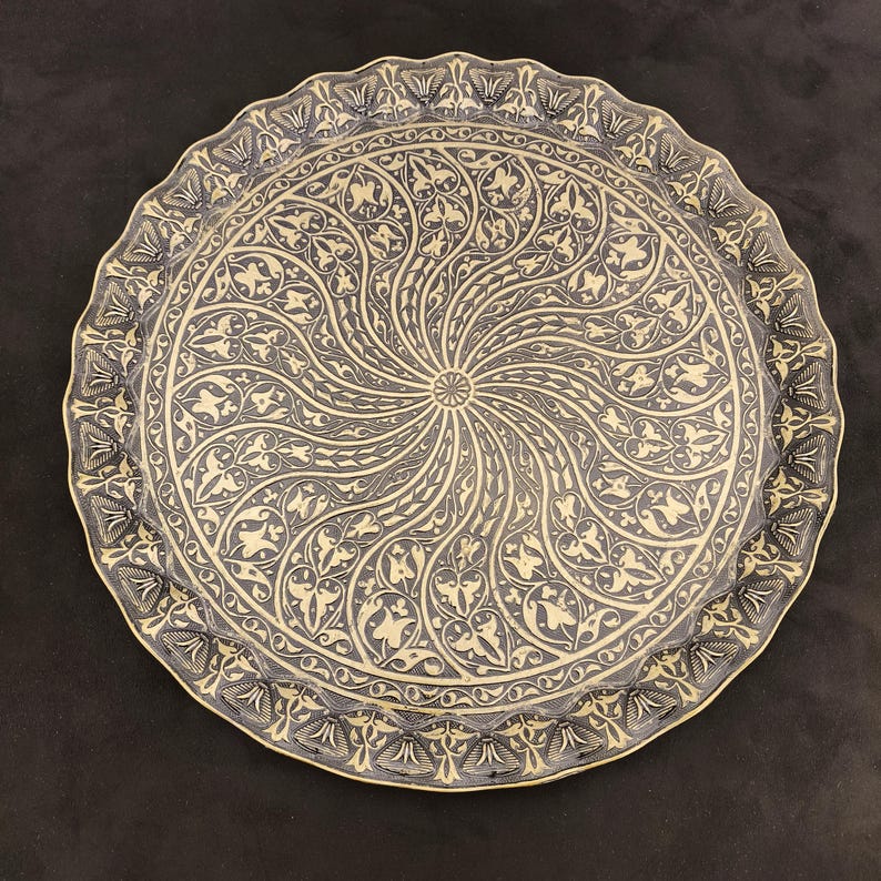 May include: A round, brass serving tray with a decorative, swirling pattern of black and gold floral designs.
