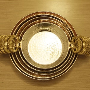 May include: A set of four nesting bowls with hammered copper and gold finishes. The bowls have decorative handles on each side.