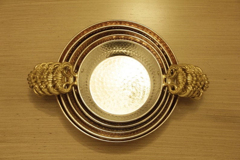 May include: A set of four nesting bowls with hammered copper and gold finishes. The bowls have decorative handles on each side.