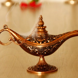 Peut inclure: Une lampe &agrave; genie dor&eacute;e avec des d&eacute;tails complexes et une poign&eacute;e en cha&icirc;ne. De la fum&eacute;e s'&eacute;l&egrave;ve du haut de la lampe.
