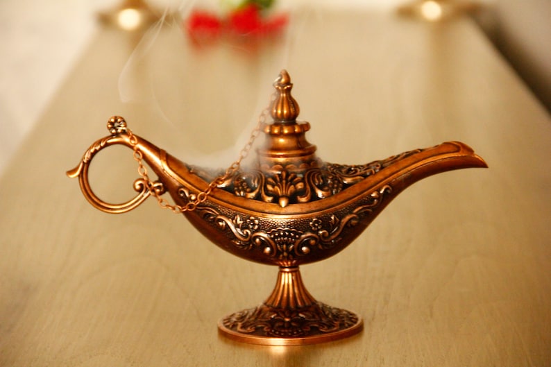 Peut inclure: Une lampe &agrave; genie dor&eacute;e avec des d&eacute;tails complexes et une poign&eacute;e en cha&icirc;ne. De la fum&eacute;e s'&eacute;l&egrave;ve du haut de la lampe.