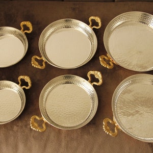 May include: Set of six silver-colored metal serving dishes with gold-colored handles. The dishes are round and have a hammered texture.