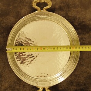 May include: A round, hammered silver serving tray with two ornate gold handles. The tray is 20 inches in diameter.