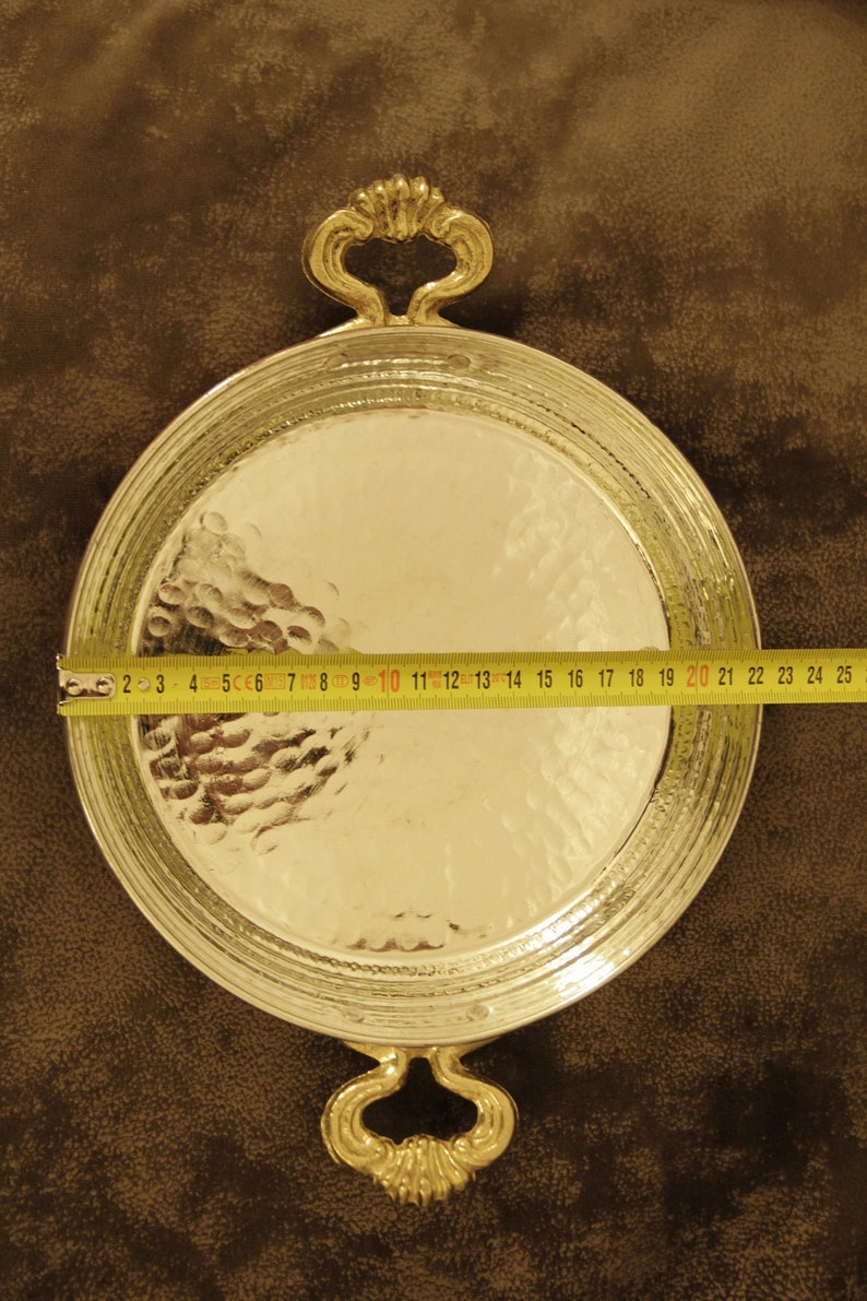 May include: A round, hammered silver serving tray with two ornate gold handles. The tray is 20 inches in diameter.