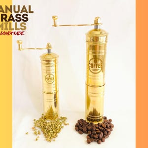 May include: Two brass manual mills, one labeled "Pepper" and the other "Coffee", with a crank handle. The mills are on a white surface with peppercorns and coffee beans. The text "MANUAL BRASS MILLS HANDMADE" is in the upper left corner.