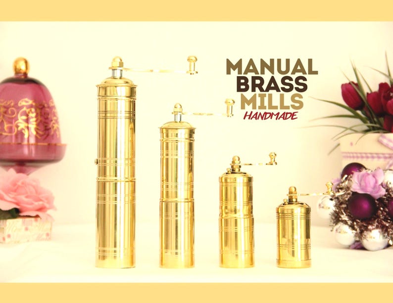 May include: Four handmade, gold-tone brass manual coffee mills of varying sizes are displayed against a light background.  The mills feature a classic design with vertical grooves. The text 'MANUAL BRASS MILLS HANDMADE' is prominently displayed above the mills.  The image showcases the craftsmanship and detail of these small kitchen tools. Brass Pepper mill. Brass coffee mill. manual grinder. manual coffee grinder. manual pepper grinder.