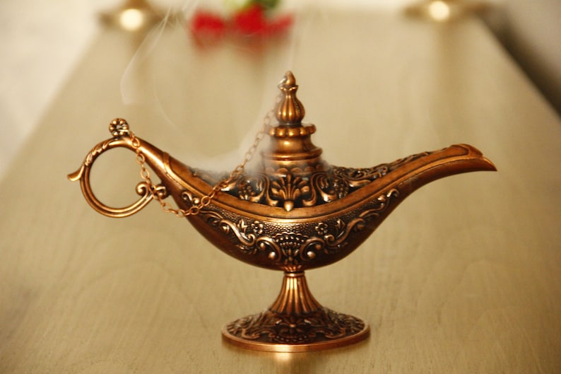 Peut inclure: Une lampe &agrave; genie dor&eacute;e avec des d&eacute;tails complexes et une poign&eacute;e en cha&icirc;ne. De la fum&eacute;e s'&eacute;l&egrave;ve du haut de la lampe.