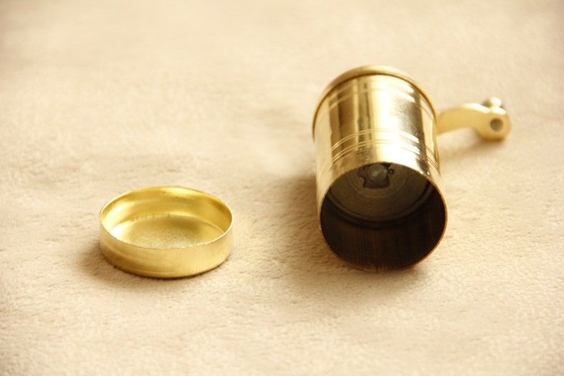 May include: A gold metal grinder with a handle and a removable lid. The grinder is used for grinding spices or other ingredients.
