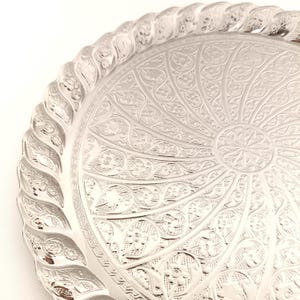 May include: A silver serving tray with a decorative, embossed design. The tray has a raised, scalloped edge.