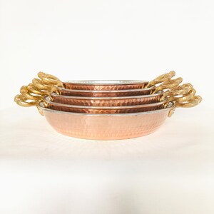 May include: Set of four copper bowls with hammered texture and gold handles. The bowls are stacked in decreasing size.