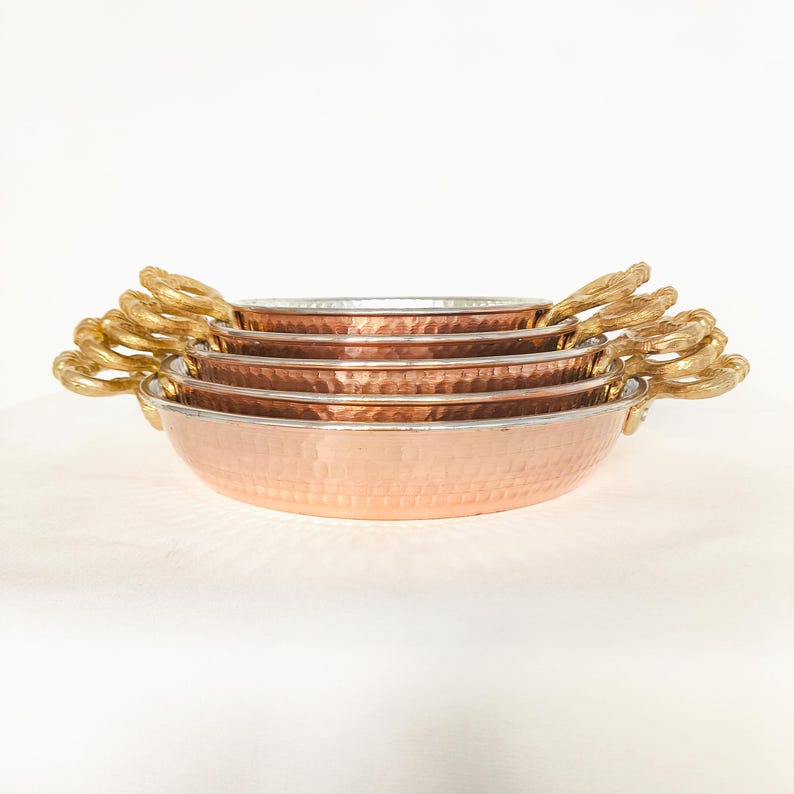 May include: Set of four copper bowls with hammered texture and gold handles. The bowls are stacked in decreasing size.