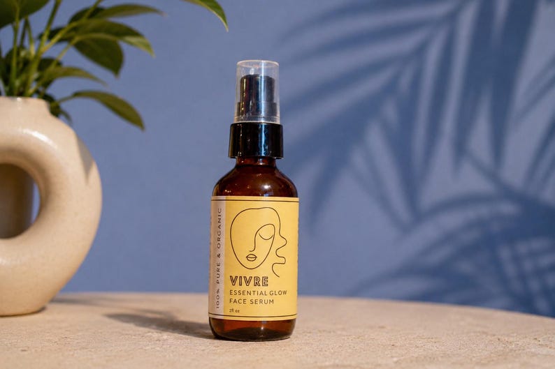 Puede incluir: Una botella de vidrio marr&oacute;n de s&eacute;rum facial con una bomba negra y una etiqueta amarilla. La etiqueta presenta la palabra "VIVRE" y el texto "ESSENTIAL GLOW FACE SERUM". La botella est&aacute; sobre una superficie clara con un fondo azul.