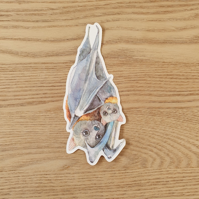 May include: A watercolor illustration of two bats hanging upside down. The bats are gray and brown with black eyes and a light blue background.