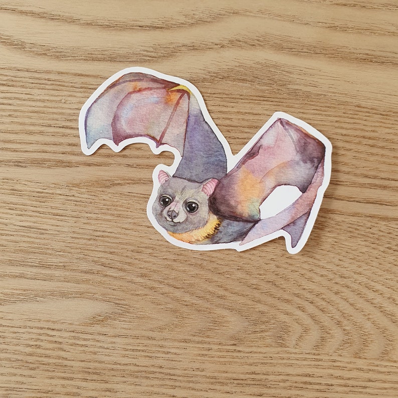 May include: A watercolor illustration of a bat with a pink, purple, and yellow wingspan. The bat has a light gray body with black eyes and a pink nose.