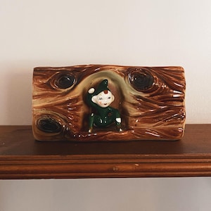 May include: A vintage ceramic planter with a whimsical elf figure in a textured wood-grain design. The rectangular planter has a brown and tan colour scheme. It is likely used for small plants or decorative purposes, and is a charming piece.
