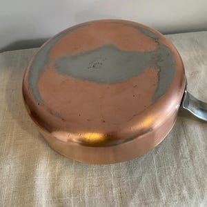 May include: A copper saucepan with a silver handle. The base of the pan shows wear and a grey interior coating. This pan is likely used for cooking and is a kitchenware item.