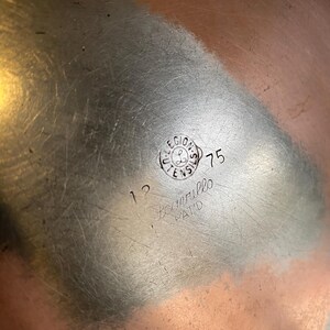 May include: A copper-coloured metal bowl with a brushed finish. The bowl features a circular stamp with the text "LEGIONS UTENSILS" and the number "75". Additional text includes "12" and "Scorrillo PAT'D".