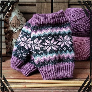 Puede incluir: Calientamanos de punto morado y negro con un patrón de copo de nieve. Los calientamanos están hechos con un hilo suave y tienen un puño de canalé.