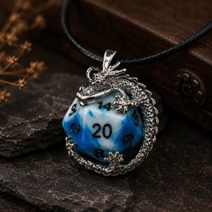 Peut inclure: Un pendentif dragon en métal argenté enroulé autour d'un dé à vingt faces avec une finition marbrée bleue et blanche. Le dé présente des chiffres noirs gravés, dont un 20 bien visible. Le pendentif est suspendu à un collier en cordon noir.