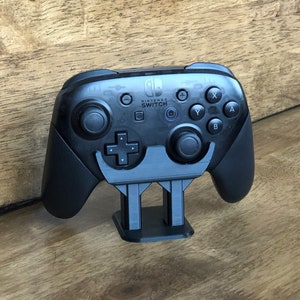 May include: A black Nintendo Switch controller is displayed on a black stand. The controller has the Nintendo Switch logo and the words "Nintendo Switch" printed on it.