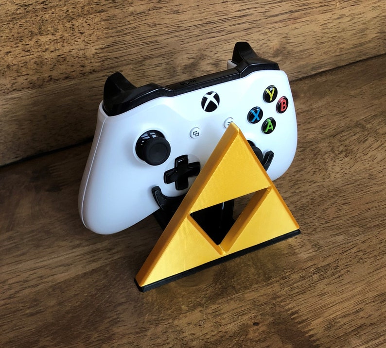 May include: A white video game controller with black buttons and a gold triangular stand. The controller has the letters X, Y, A, and B on the buttons.