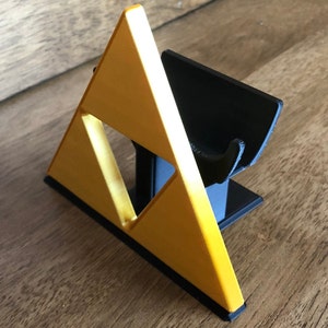 May include: A 3D printed stand for a video game console controller, shaped like the Triforce from the Legend of Zelda video game series. The stand is made of black and gold plastic.