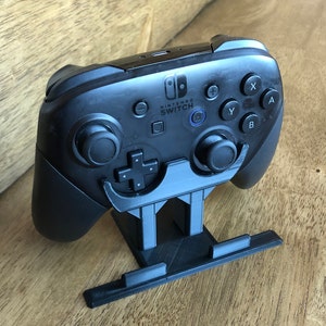 May include: A black Nintendo Switch Joy-Con controller is mounted on a black plastic stand. The controller has buttons labeled A, B, X, Y, and +.