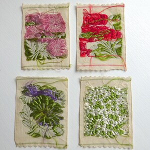 以下が含まれることがあります： 花柄の刺繍が施された小さな布の正方形が4つ。正方形はピンク、赤、緑、紫の色合いです。