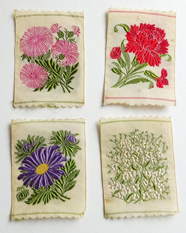 以下が含まれることがあります： 花柄の刺繍が施された布の正方形が4つあります。最初の正方形には、緑の葉が付いたピンクの花が描かれています。2番目の正方形には、緑の葉が付いた赤い花が描かれています。3番目の正方形には、緑の葉が付いた紫の花が描かれています。4番目の正方形には、緑の葉が付いた白い花が描かれています。