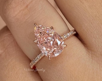 May include: A pear-shaped light pink gemstone ring set in a rose gold band with small pavé diamonds along the shank. The ring features a prominent central stone held by four prongs. The text Vitara Jewelry is visible on the band near the setting.
