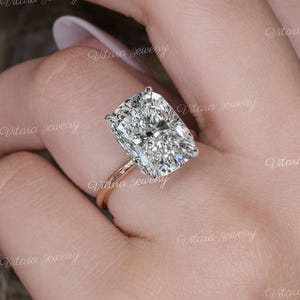 May include: A rose gold ring with a large, rectangular-cut diamond. The diamond is clear and multifaceted, reflecting light. The ring is set on a delicate band, highlighting the gemstone's brilliance. The image is branded with the text "Vitara jewelry".