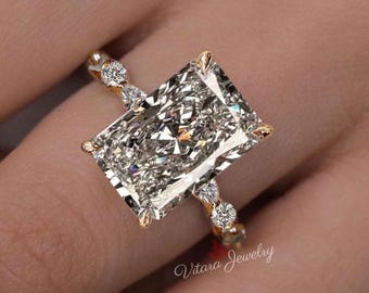 May include: A rose gold ring featuring a large rectangular radiant-cut center stone held by four prongs. The band is accented with a series of small round and marquise-cut diamonds on each side. The text Vitara Jewelry is visible in the corner.